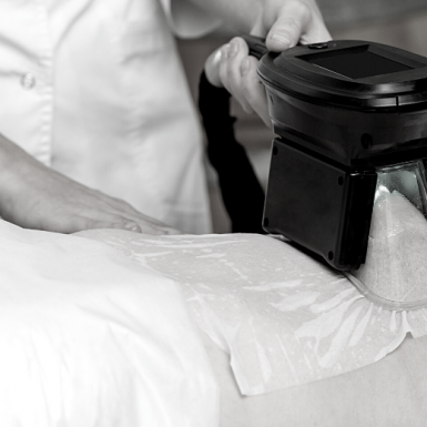 A CoolSculpting device in use, designed for non-invasive fat reduction by freezing fat cells, being applied to a client's body part covered with a protective gel pad.