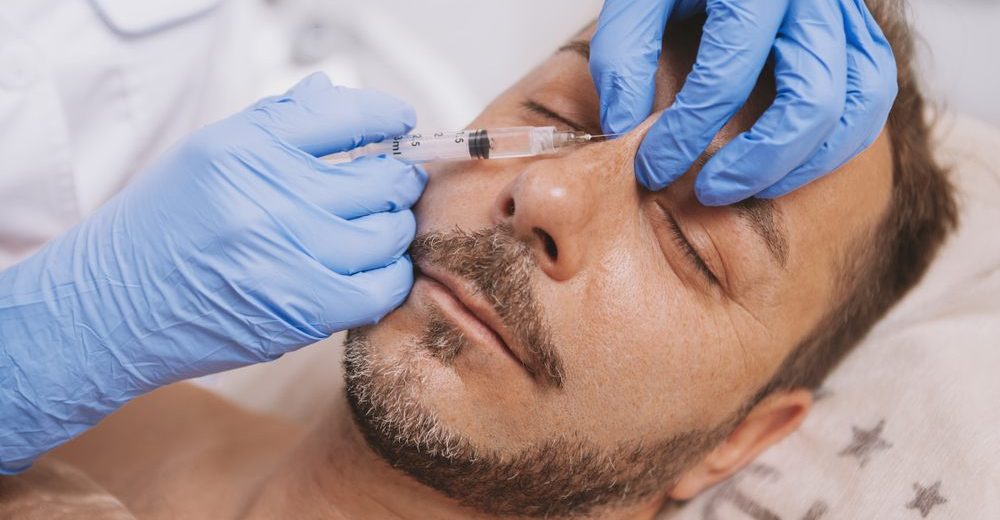 Male patient receiving dermal filler injection for non-surgical rhinoplasty nose reshaping